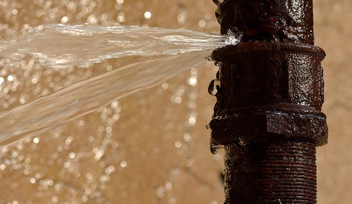 rusty burst pipe squirting water at high pressure